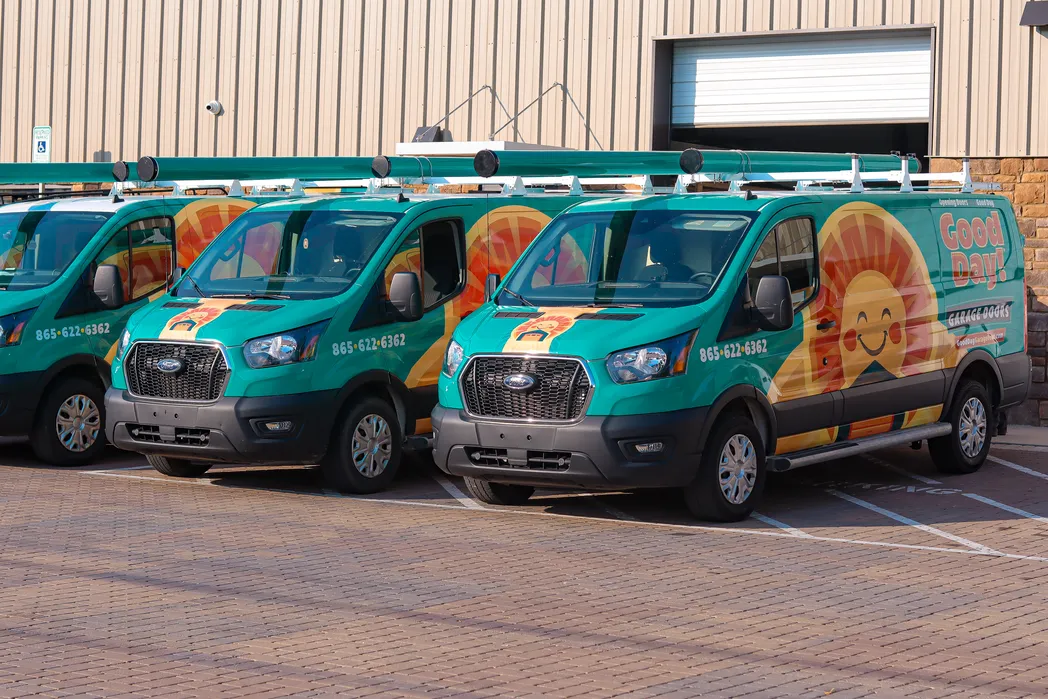 Three Good Day Garage Doors Ford Transit vans in matching wraps parked outside a metal warehouse building.